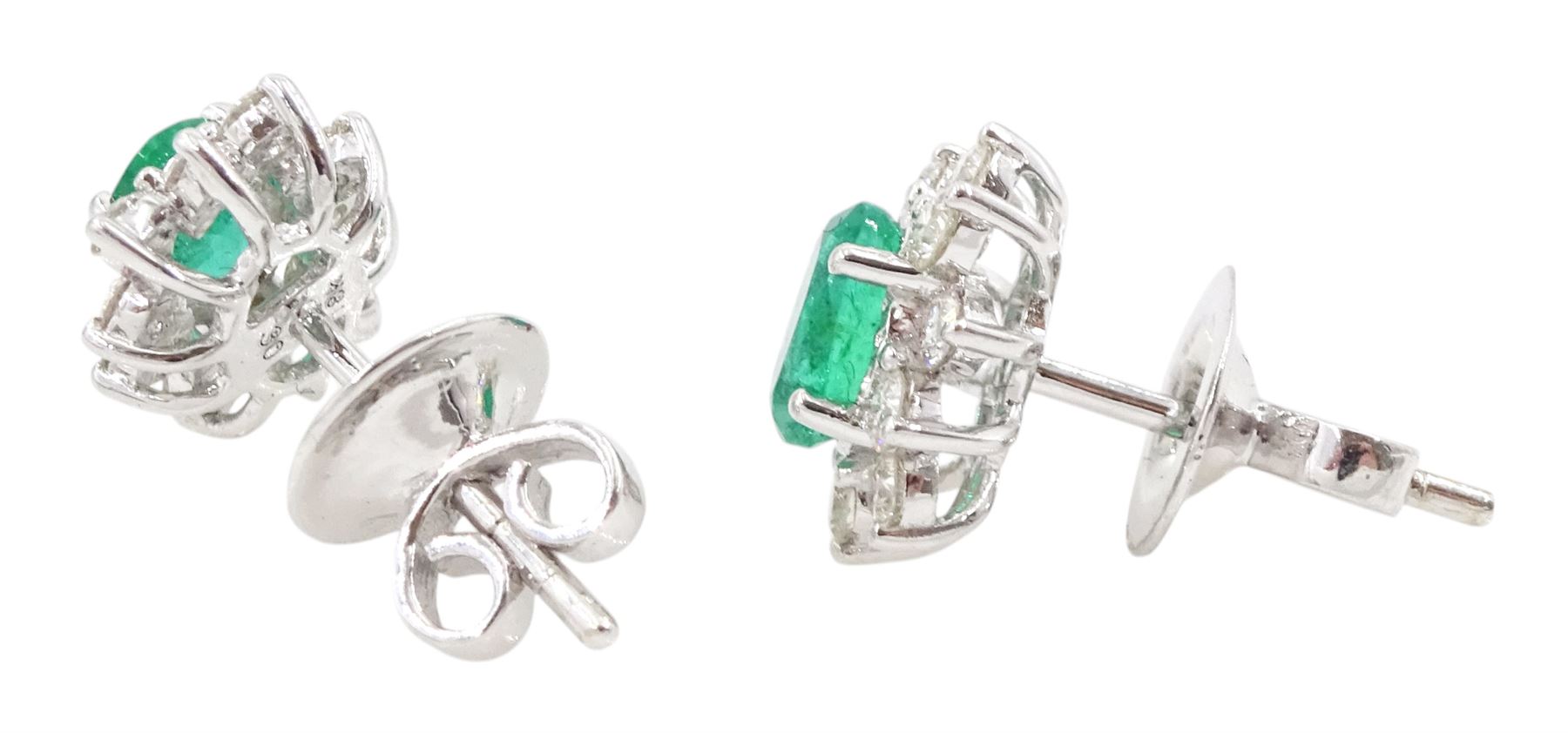 Pair of 18ct white gold emerald and diamond stud earrings, each cluster set with a single oval cut emerald surrounded by ten round brilliant cut diamonds, stamped, total emerald weight approx 0.80 carat, total diamond weight approx 0.55 carat