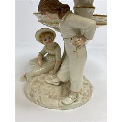 Royal Worcester figural double comport in the style of Kate Greenaway, modelled with a young boy and girl with painted features beside an oak tree stump branching out to support the two basket woven style dishes, raised upon rocky circular base, decorated with gilt detail throughout, with green printed stamp mark and impressed marks beneath, H19.5cm