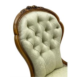 Victorian walnut framed nursing chair, the cresting rail decorated with carved applied flower heads and acanthus leaves, shaped back and sprung seat upholstered in buttoned ivory damask fabric, serpentine front over cartouche carved cabriole supports with ceramic castors (W57cm H92cm); with matched footstool, circular top over shaped moulded apron, on floral carved cabriole feet (W34cm) 