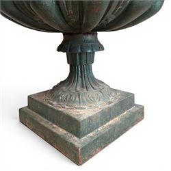 Pair of Victorian cast iron campana garden urns, the flared rim with repeating stylised anthemion motifs with scrollwork, over a deep gadrooned and Aesthetic moulded underbelly, fluted and foliate lower bowls on square pedestal bases, in antique green-painted finish