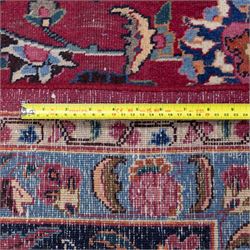 Persian Mashad design wool carpet, the red ground with dense scrolling floral and foliate decoration, within dark blue main border decorated with repeating palmettes and shaped leaves