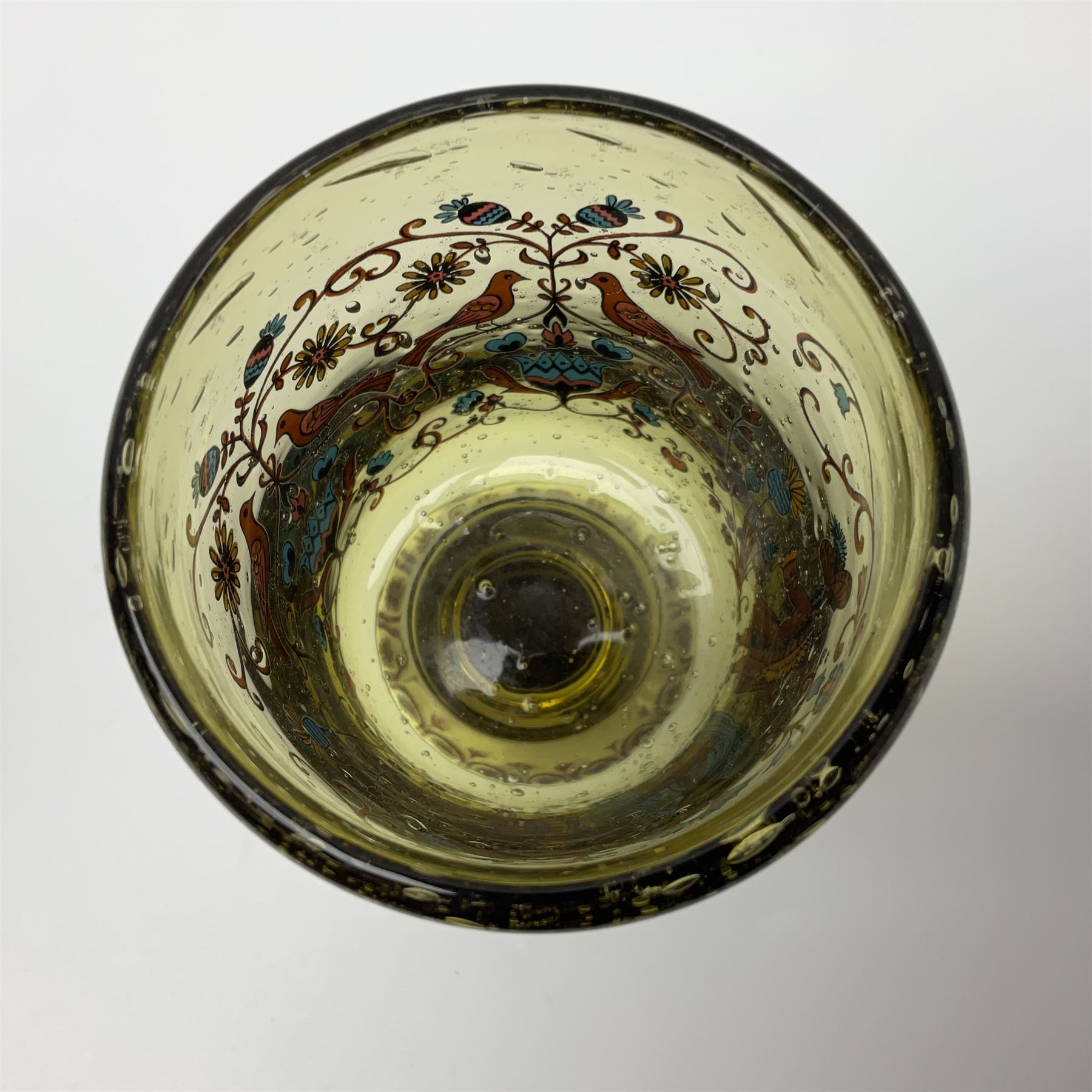 19th Century Bohemian amethyst glass lidded goblet, the bowl of faceted form, gilded with three children in period dress playing games, upon a knopped stem and conforming faceted foot, together with an art nouveau green glass goblet, with gilded rim, upon clear trumpet stem, and a hand blown wine glass, transfer printed with birds and three figures in period dress, tallest H29cm