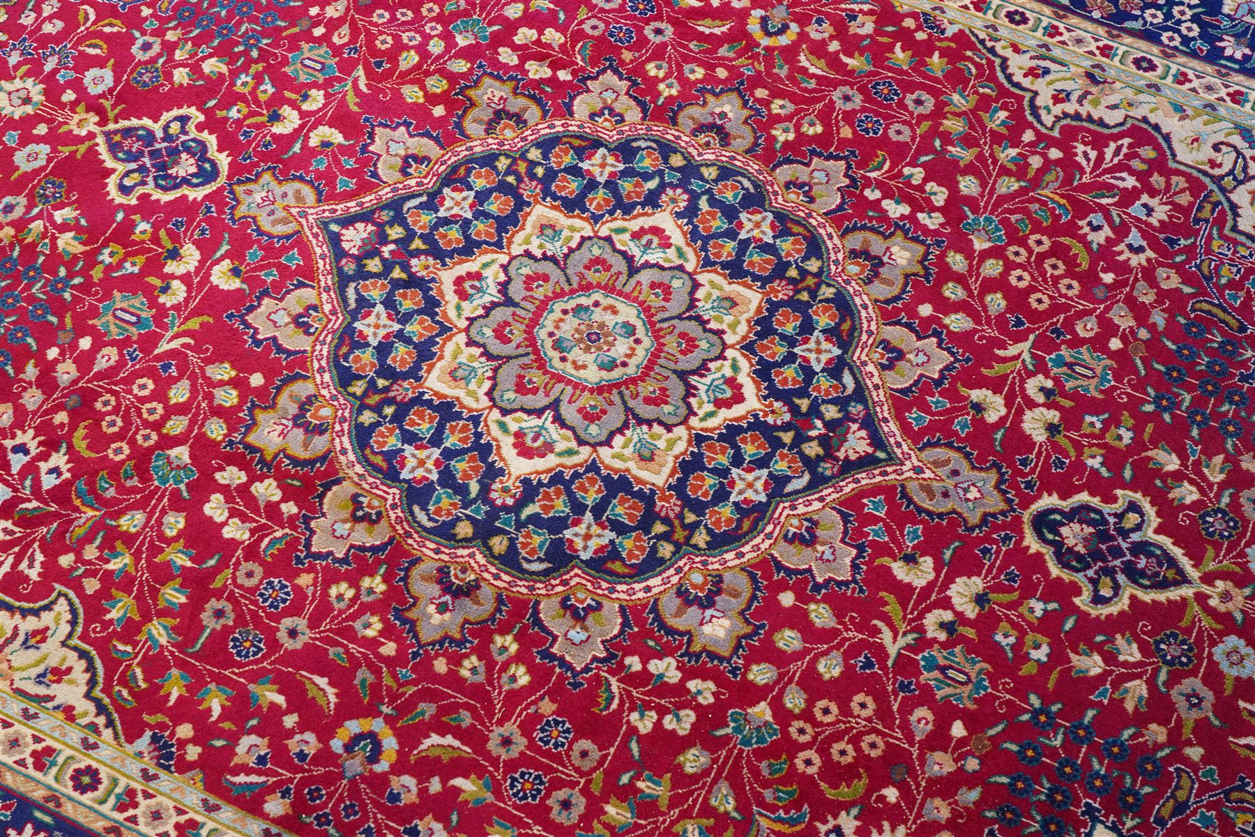 North West Persian Tabriz hand-knotted carpet, madder red field with a central cusped medallion issuing radiating pendants and an all-over design of scrolling arabesques, palmettes and flowering vinery enclosed by conforming spandrels, indigo main border of meandering floral vines and stylized palmettes, flanked by narrow guard stripes, cotton fringe ends 