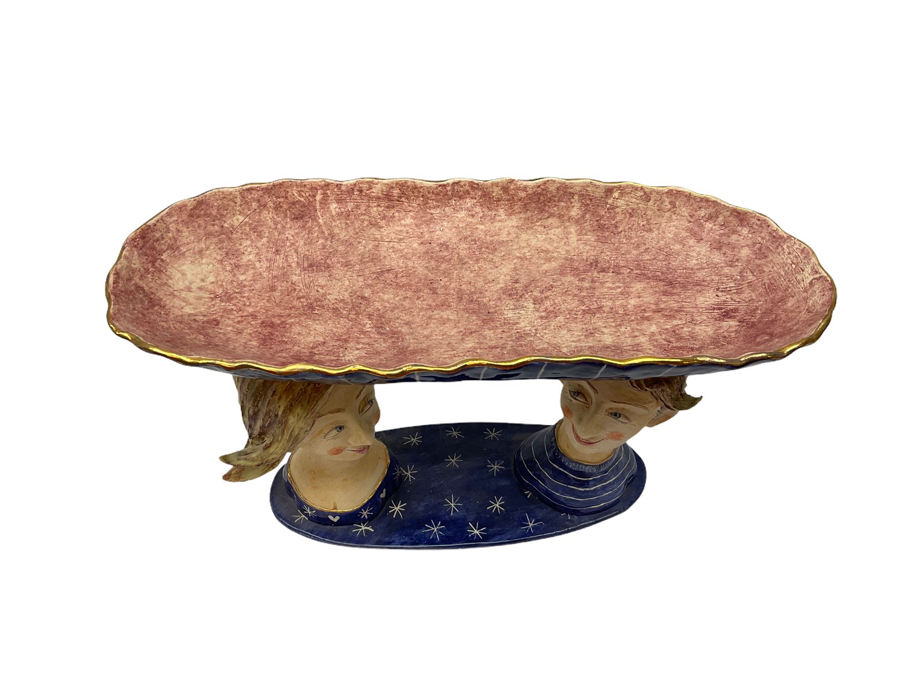 Ceramic 'girl and boy dish', by Helen Kemp, an oval dish with a mottled pink ground and gilt edging upon the sculpted heads of a girl and a boy, together with a 'boy sconce', by Helen Kemp, a sculpted boy holding a small bowl with foliate decoration, both with the artist's mark beneath.