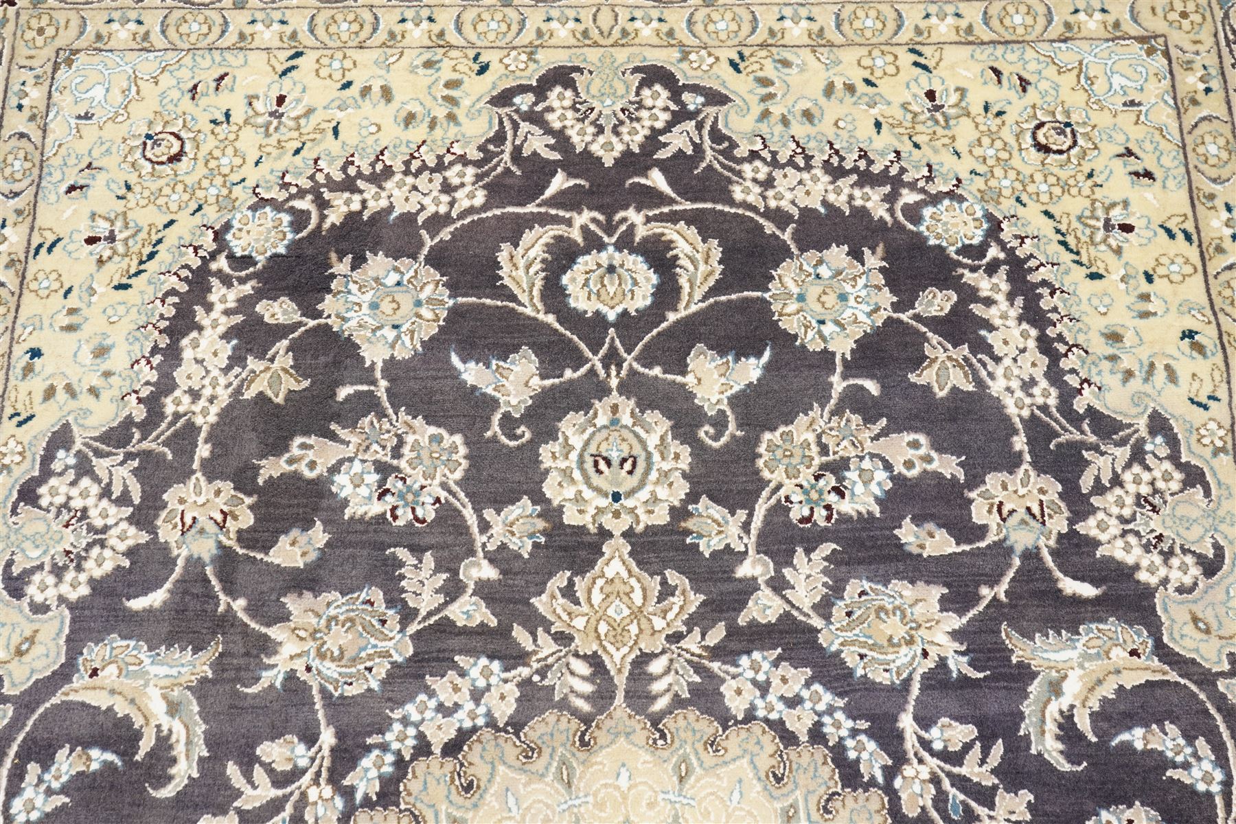 Central Persian Nain hand-knotted carpet, indigo field with central cusped medallion of radiating palmette form, enclosed with an elongated cartouche issuing network of scrolling vine work, arabesques and flowering sprays, surrounding ivory field of conforming design filled with foliate motifs and palmettes, spandrels of complimentary design with angular reserves, within principal border of ivory ground with scrolling vinery rosettes and arabesques, flanked by narrow guard stripes, with cotton fringe ends 