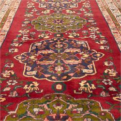 North West Persian Tariz hand-knotted runner, madder red field with a column of linked lozenge medallions in shades of indigo blue and pistachio green framed by stylized floral motifs within triple borders of rosettes and scrolling vines on an ivory ground, with cotton fringe ends
