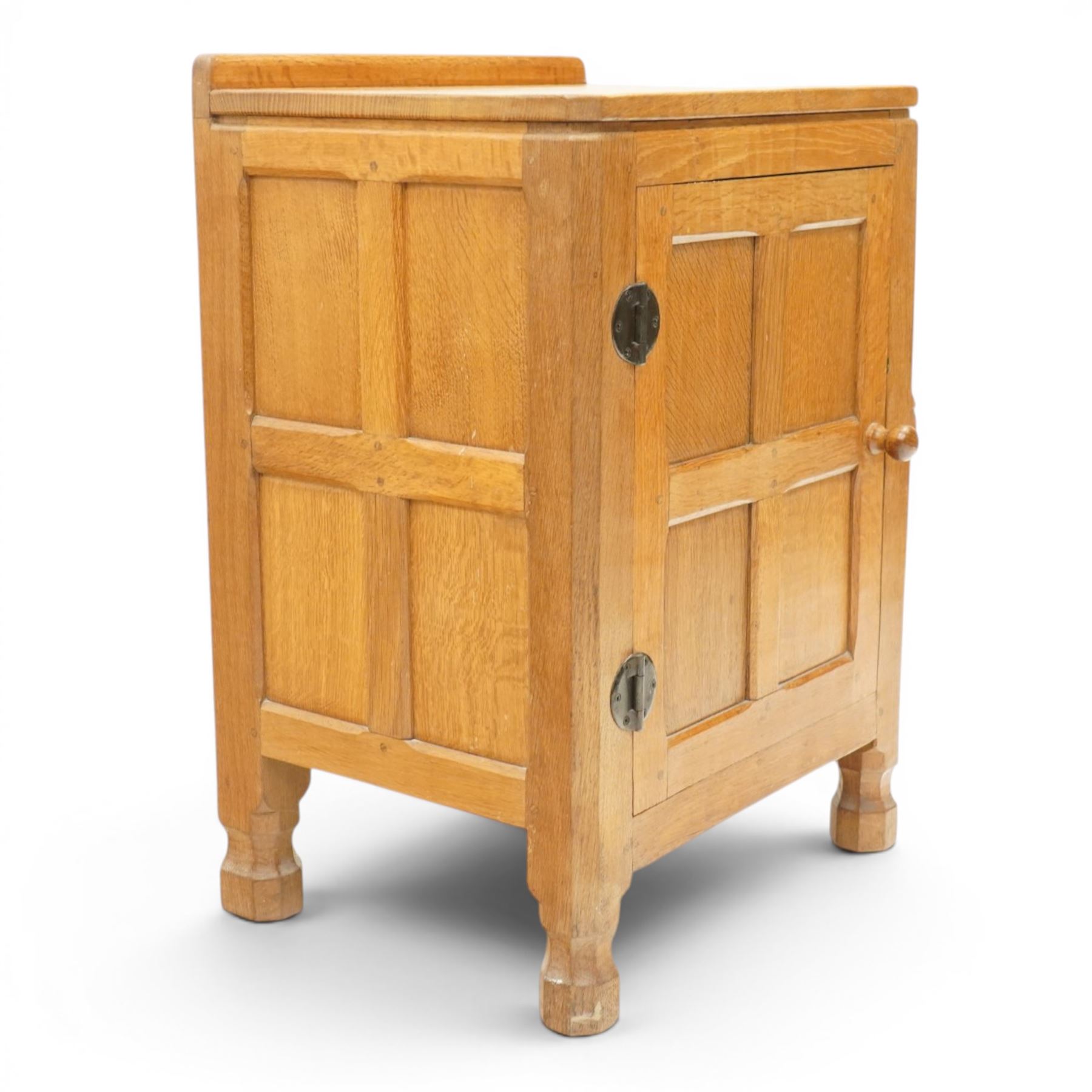 Mouseman - adzed and panelled oak bedside cupboard of small proportions, raised back over rectangular canted top, fitted with single panelled cupboard door with chamfered rails and turned knob handle, enclosing single shelf, raised on octagonal feet,  carved with mouse signature, by the workshop of Robert Thompson of Kilburn