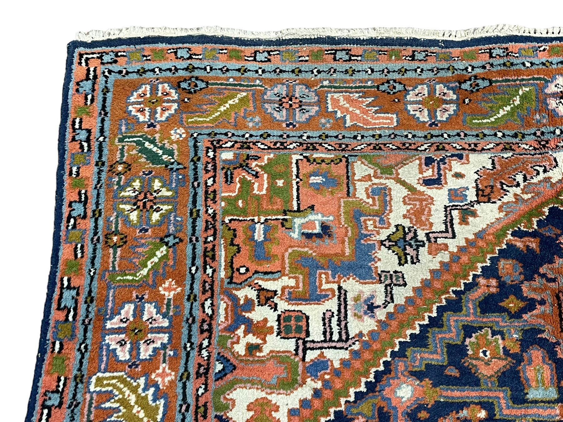 Persian Heriz indigo and rust ground rug, central geometric star medallion decorated with stylised foliate motifs, the border decorated with stylised flower heads