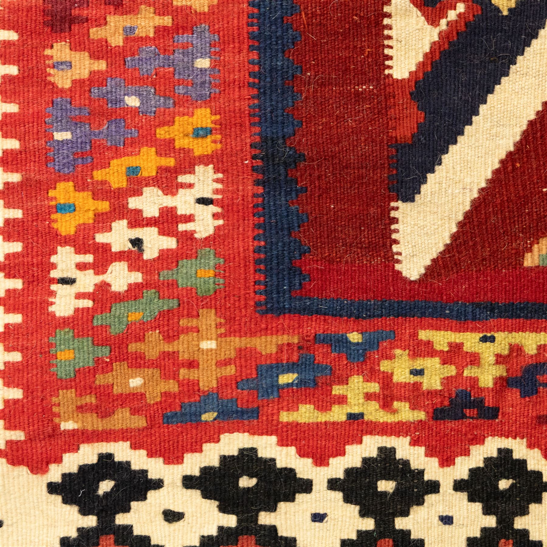 South West Persian Qashqai flatweave kilim, madder red ground with stacked diamond panels filled with latch hook and angular floral motifs, enclosed by multiple geometric borders in palettes of indigo, green, and ochre 
