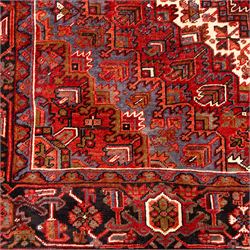 North West Persian Heriz hand-knotted carpet, madder red field, with a large central angular star medallion with stepped outlines on ivory ground, surrounded by geometric floral devices and stylized rosettes, with corresponding corner spandrels, enclosed by a bold geometric main border with multiple guard stripes, with cotton fringe ends 