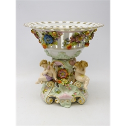  German Sitzendorf porcelain centrepiece, the pierced basket applied with fruit and trailing flowers, the stem supported by three cherubs on scrolled supports, H31cm   