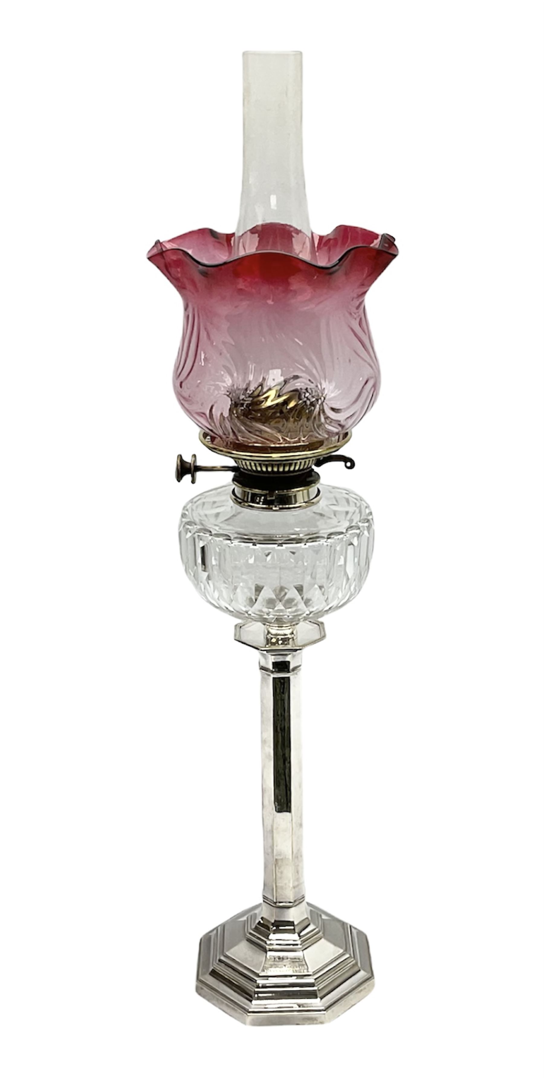 20th century Hawksworth, Eyre & Co silver plated oil lamp, the octagonal stepped base with engraved dedication, leading to an octagonal column supporting a faceted clear glass reservoir, Hinks Duplex burner, clear glass chimney, and cranberry glass shade, overall H71.5cm