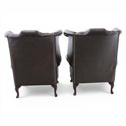 20th century Chesterfield style brown leather wingback armchairs, with button upholstered backs and wings, shaped scroll arms with studded borders, loose seat cushions, raised on cabriole supports with pad feet