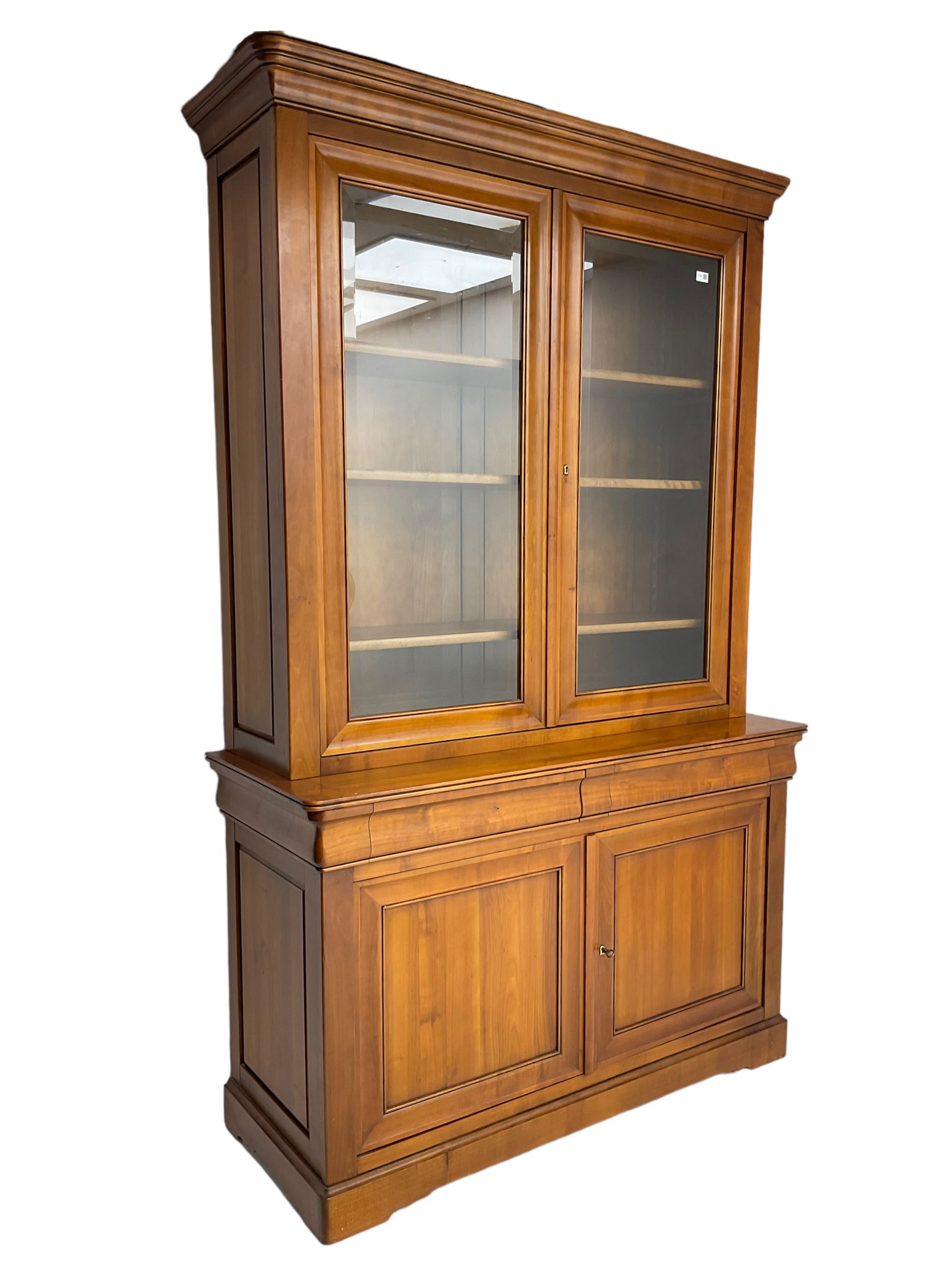 French cherry wood bookcase on cupboard, projecting cornice over two cupboard doors with bevelled glass panels enclosing three adjustable shelves, base fitted with two cushion drawers over double cupboard
