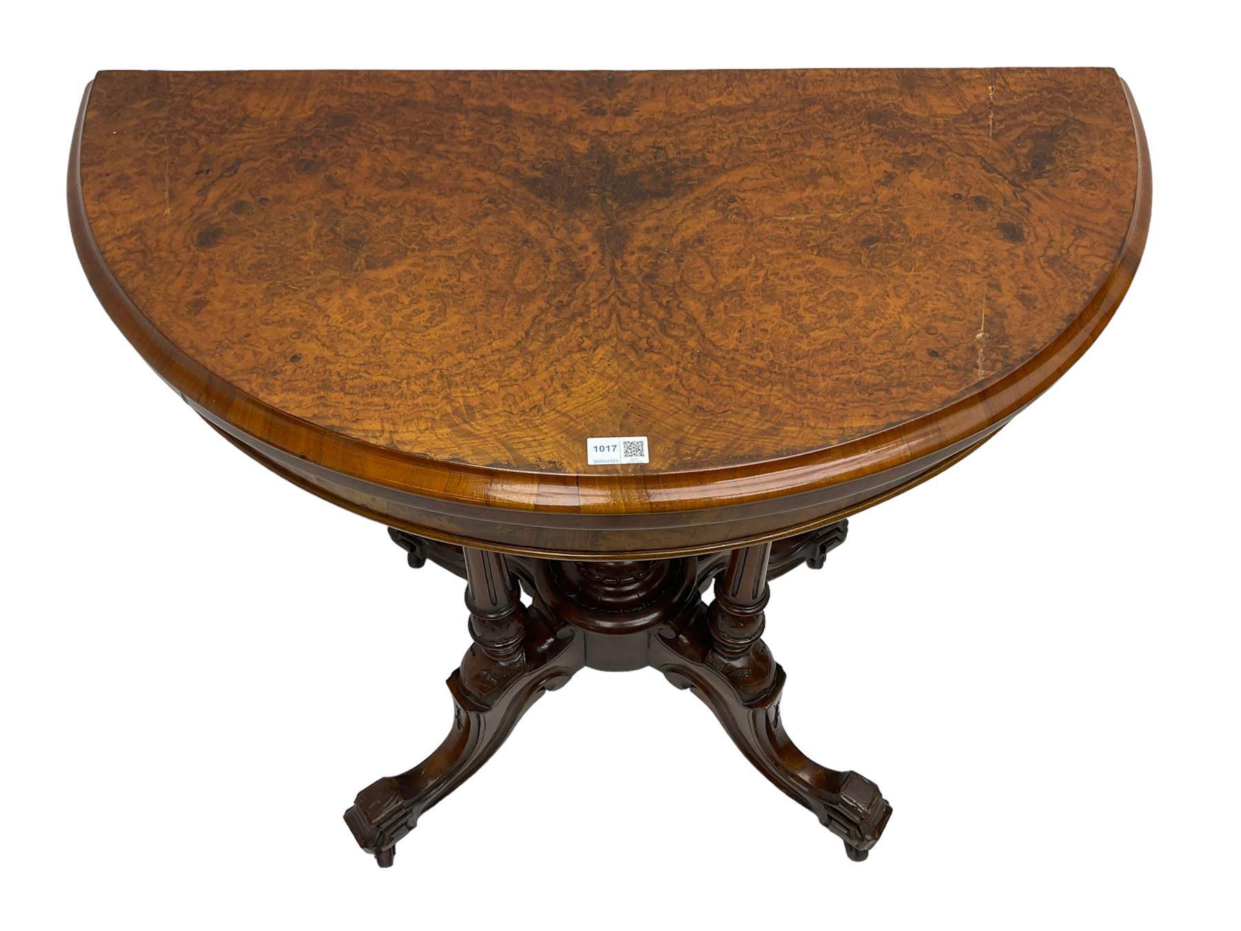 Victorian figured walnut demi-dune card table, the fold-over moulded top with circular baize lining, on four turned pillars with central finial platform, four splayed moulded supports with angular scrolled feet, on castors