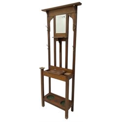 Edwardian oak hall stand, raised back with rectangular bevelled mirror plate surrounded by shelf and coat hooks, fitted with a glove box with hinged lid, over an undertier with two inset umbrella drip trays