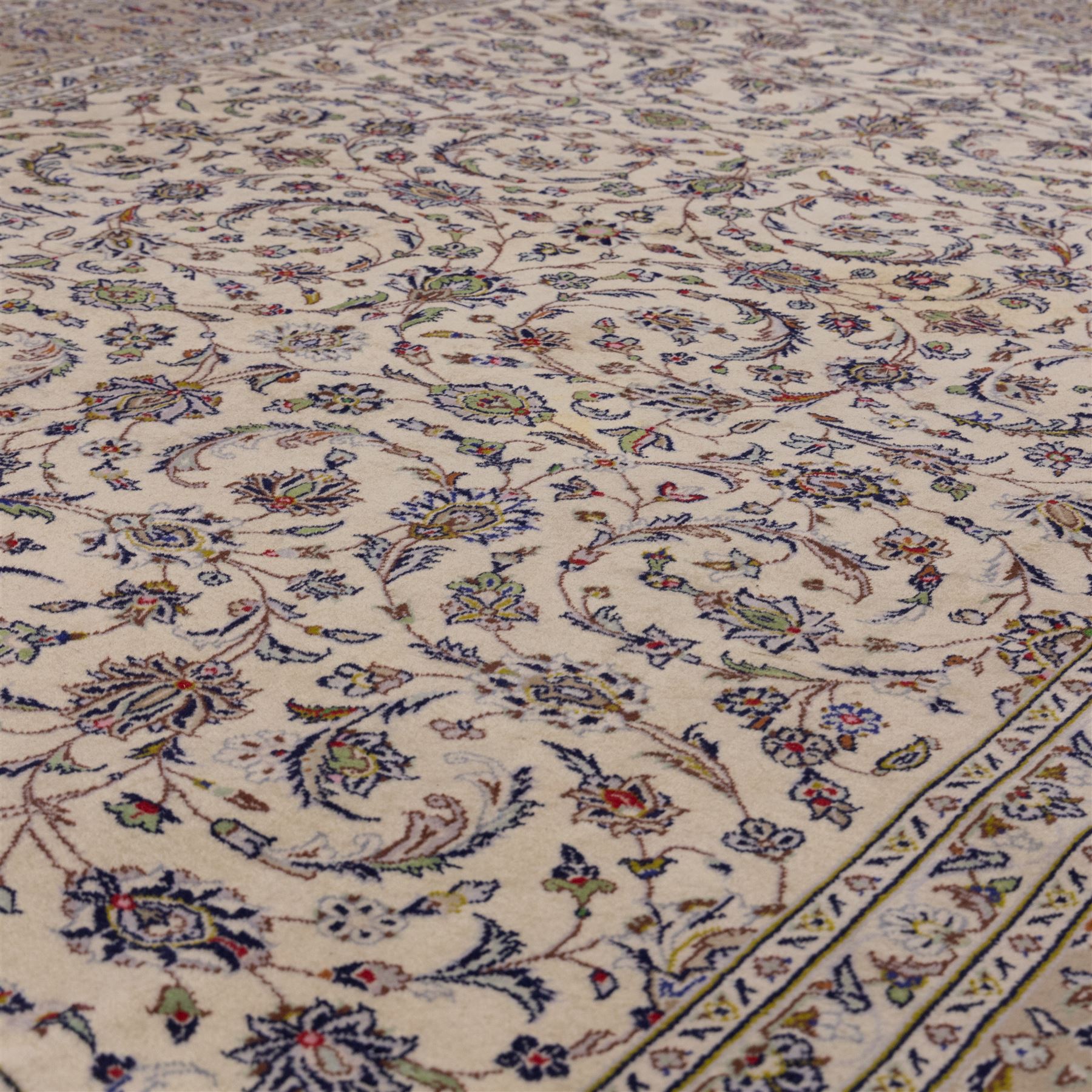 Central Persian Kashan hand-knotted carpet, ivory field densely decorated with an all-over design of scrolling floral vines and palmettes, framed by multiple borders with continuous floral meander and rosette motifs, in a palette of indigo, ivory, soft blue, sage green, rose and ochre tones, with cotton fringe ends 