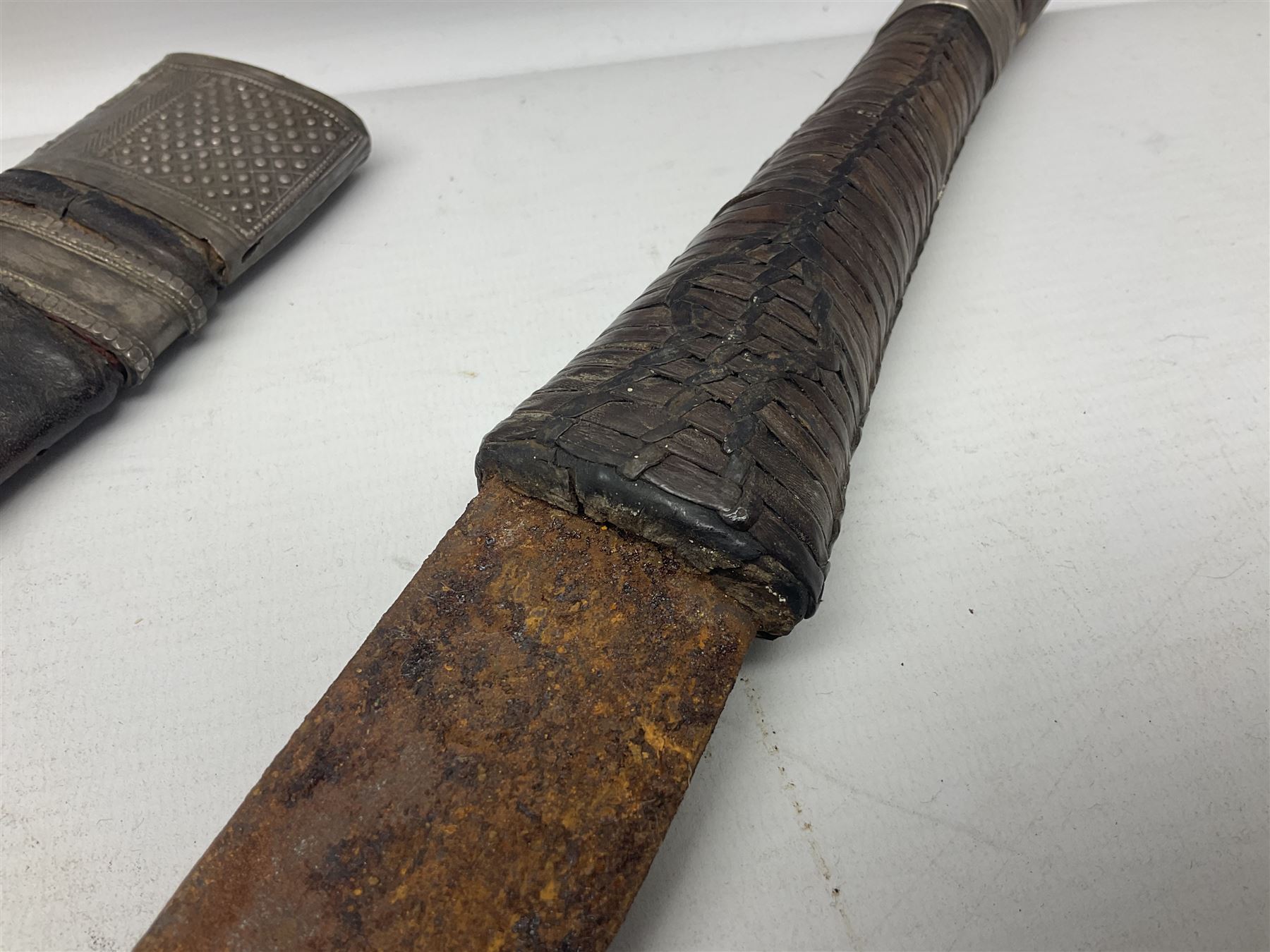 Omani presentation sword kattara, with 77cm  broad slightly curved single edge blade with two fullers, leather bound hilt woven with silver wire decoration and iron pommel;  in tooled leather scabbard with chased silver mounts and presentation plaque 'To Capt. D.M. Naylor From C Company NFR Oman Dec 1962' (Northern Frontier Regiment) L99cm overall