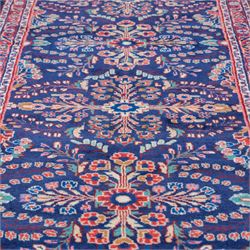 North West Persian runner, the indigo field decorated with repeating symmetrical floral sprays, rosettes and curling foliage in coral, ivory and pale blue tones, enclosed by a red ground trailing flowerhead border and narrow patterned guard bands 