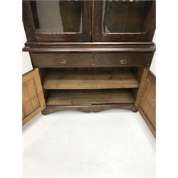Late Victorian stained pine bookcase on cupboard, projecting on cornice, two glazed doors enclosing four shelves above two drawers and two cupboards, shaped platform base, W115cm, H212cm, D40cm