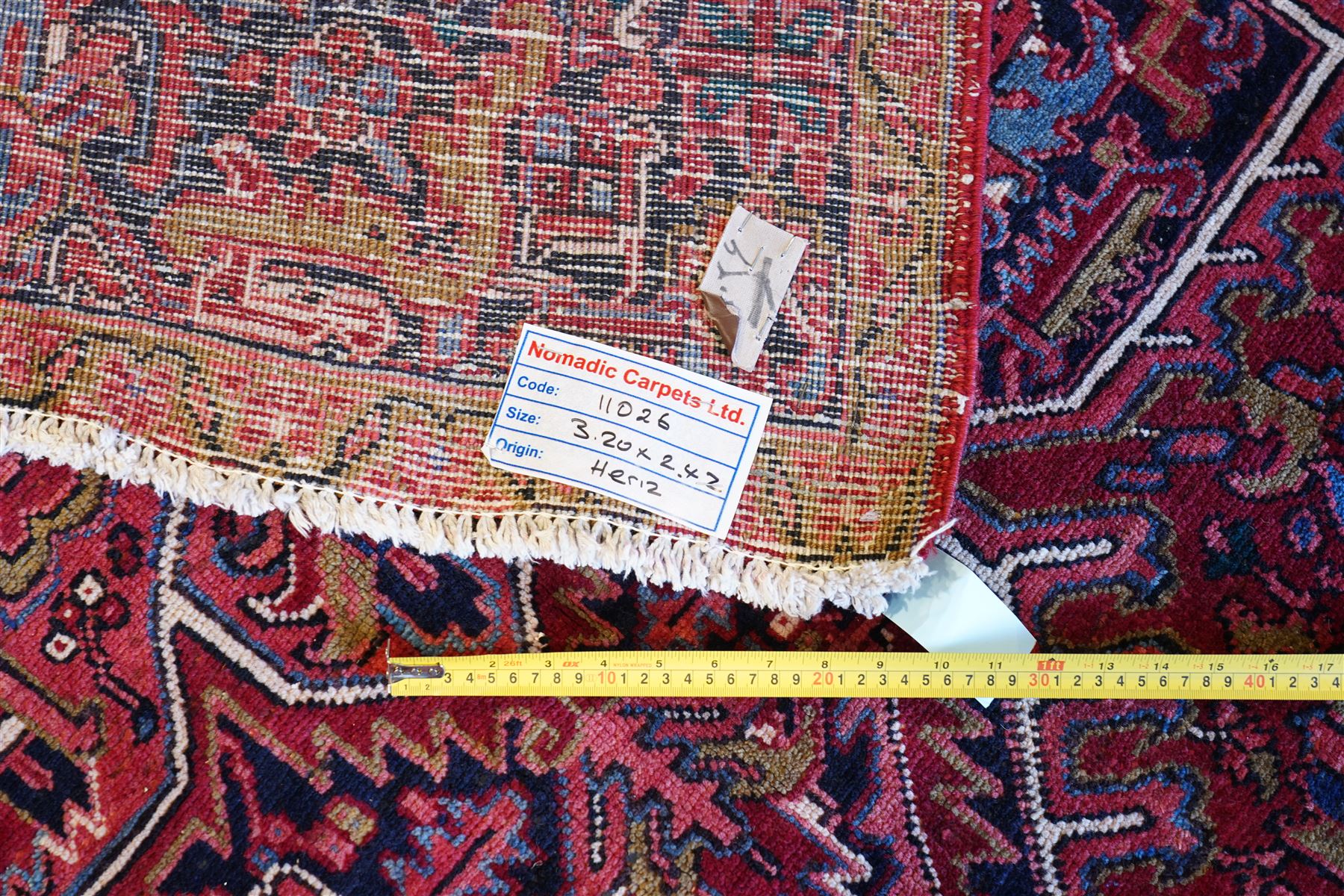 North West Persian Heriz hand-knotted carpet, brick-red field with a large central angular star medallion with pendant motifs, surrounded by stylized geometric palmettes, serrated leaves and tribal devices, ivory corner spandrels similarly decorated, field enclosed by a dark indigo main border of stylized rosettes and angular vine motifs between multiple guard stripes, with cotton fringe ends  