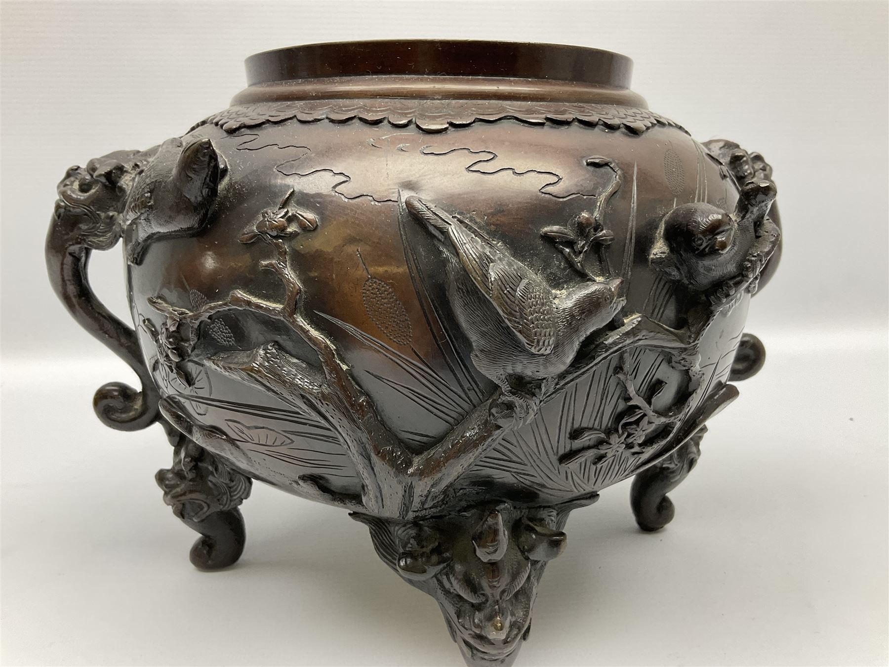 Japanese bronzed koro, the body of globular form with twin cast zoomorphic mask handles, decorated in relief with birds upon blossoming branches, against a ground incised with rushes and peonies, the flat toped domed cover with pierced band and surmounted by a cast figure of a Foo dog, the whole upon three zoomorphic mask feet, with impressed character type mark beneath, H35.5cm