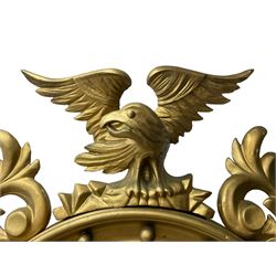 Pair of Regency period giltwood convex wall mirrors, moulded circular frame decorated with spherical mounts surmounted by a carved eagle with spread wings, foliage scroll carved upper and lower brackets, reed moulded and ebonised slip enclosed convex mirror plate 