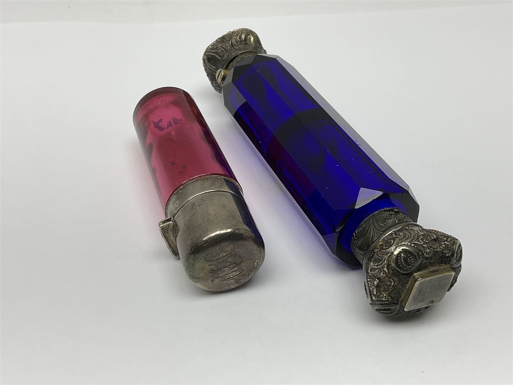 Late Victorian silver mounted ruby glass cylindrical scent bottle, with interior glass stopper, Birmingham 1900, makers mark worn, H8cm, together with a Victorian double ended cut blue glass perfume bottle mounted with white metal screw and flip caps decorated with foliate repousse detailing, H13.5cm