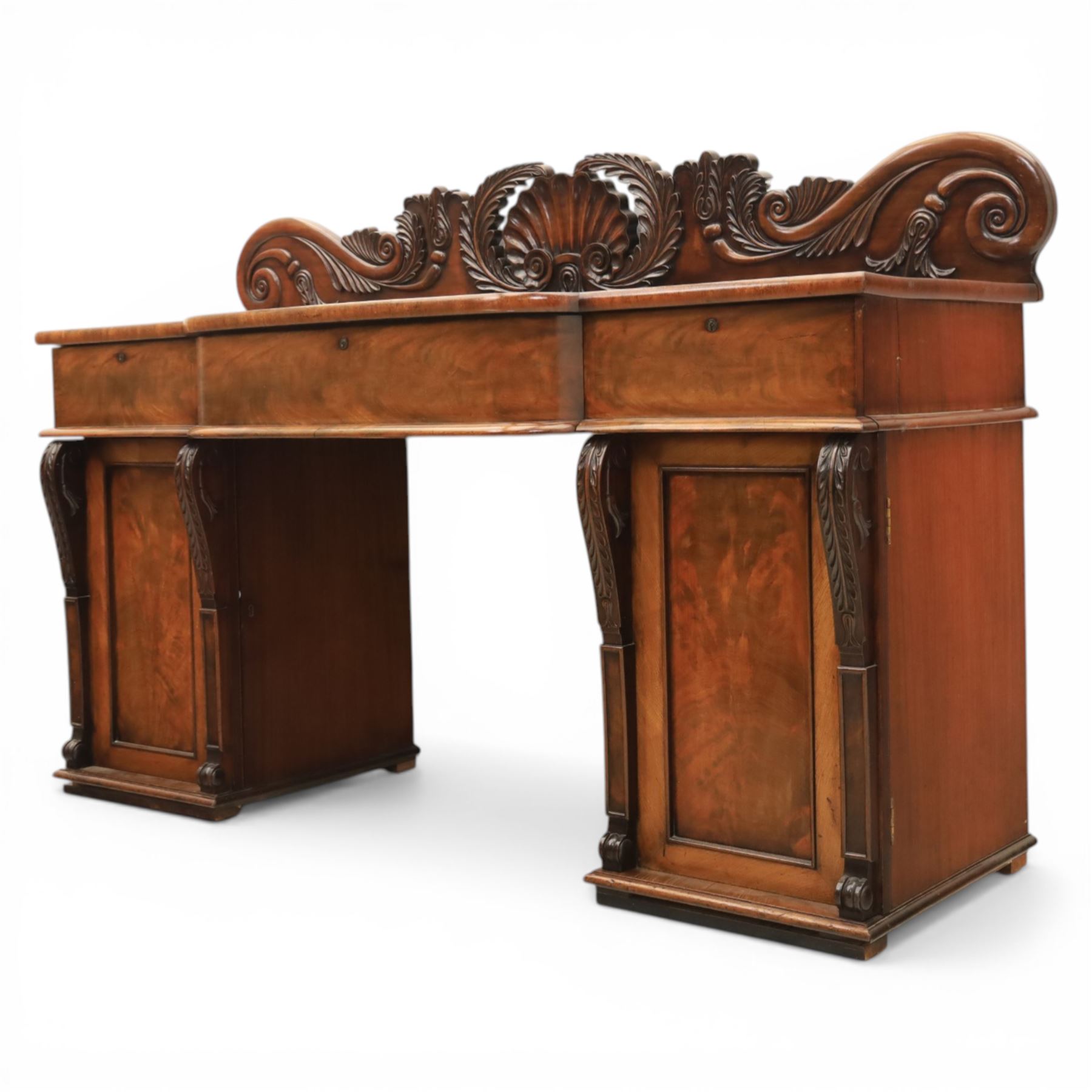 Mid Victorian mahogany pedestal sideboard, the rectangular top with raised back centred by a carved shell within scrolling acanthus and foliate cresting, over a central shaped frieze drawer flanked by two short drawers, above a kneehole recess, flanked by panelled cupboard doors with carved corbel supports, enclosing shelved interiors