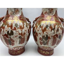 Pair of Japanese Meiji period Kutani vases, of twin handled baluster form finely painted with dense panels of figures and flowers upon foliate gilt decorated iron red ground, both with dragon mask ring handles, with red script mark beneath, together with a further matching smaller example, tallest H35cm