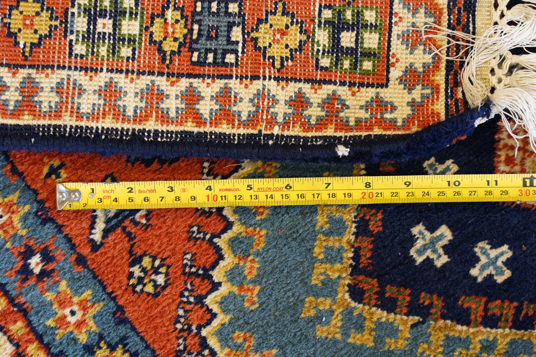 Caucasian Kazak vermillion ground rug, the sectioned field decorated with three geometric lozenge medallions surrounded by stylised plant and animal motifs, the multiple guard bands with repeating geometric design
