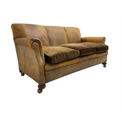 Early-to-mid-20th century three seat sofa, upholstered in worn tan leather with studwork, loose cushions upholstered in brown fabric, on compressed bun feet with castors