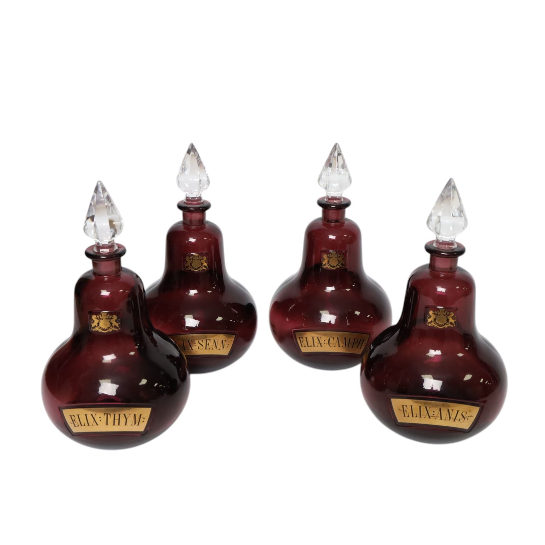 Set of four 20th century Royal Pharmaceutical Society amethyst glass bottles, of bellied form with clear cut glass spire stopper, each body bearing gilt label in Latin: ELIX:THYM:, ELIX:CAMPH:, ELIX:ANIS: and ELIX:SENN:, and gilt Royal Pharmaceutical Society crest to neck, H25cm

Provenance: From the collection of the family of Peter Green, a practising pharmacist whose career spanned the mid to late 20th century. During his professional life he managed pharmacies in Yeovil, Somerset, and later Selles Chemist in Filey, North Yorkshire, before purchasing and running his own business, Peter Green Pharmacy, located in the Market Place, Malton. The bottles were displayed as part of the traditional shop fittings in both the Filey and Malton pharmacies and were retained as part of his collection.
