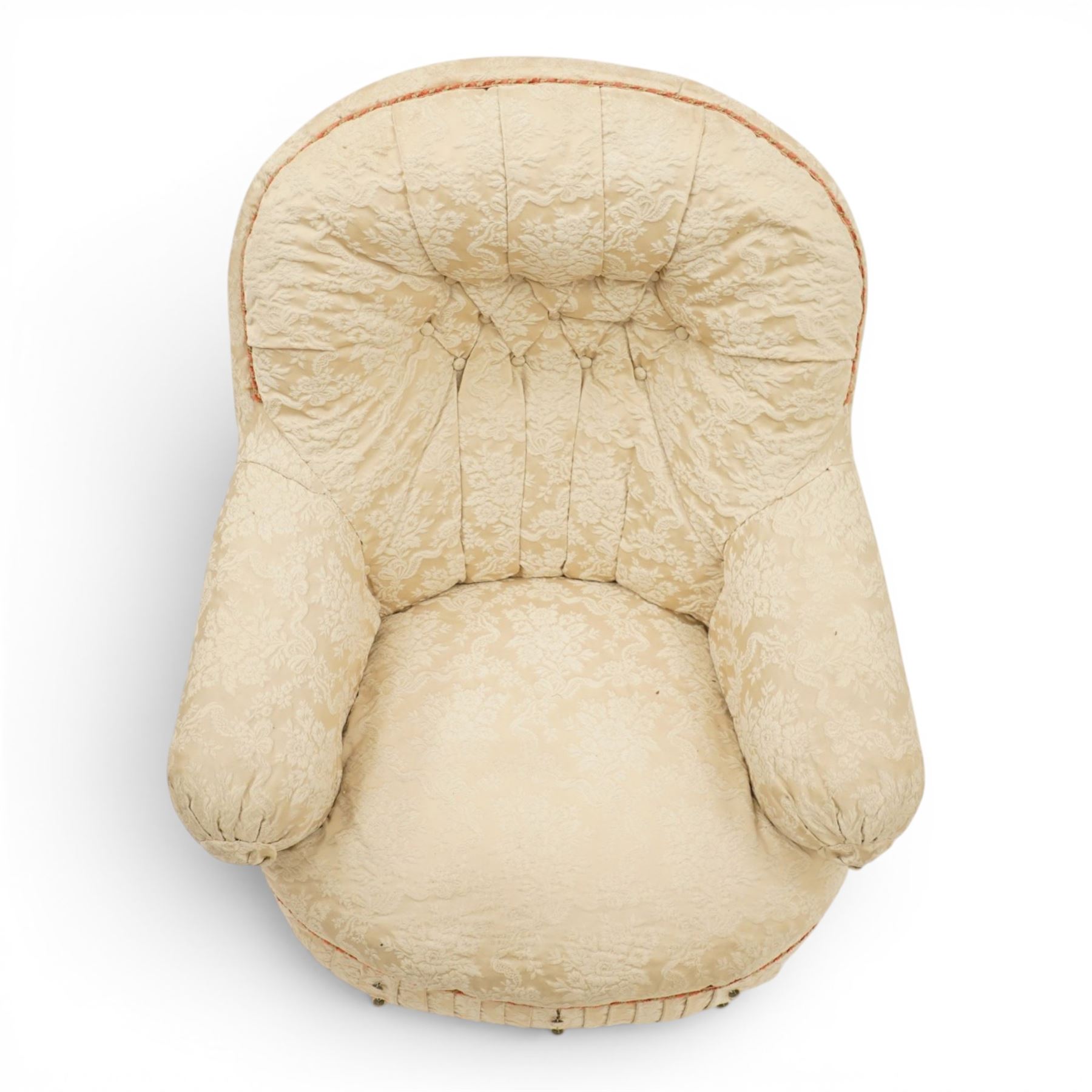 Victorian button-back nursing chair, the rounded horseshoe back enclosing a deep upholstered seat, padded arms and sprung seat in cream floral damask fabric, with crimson piping and tasselled lower fringe, on turned front legs with castors