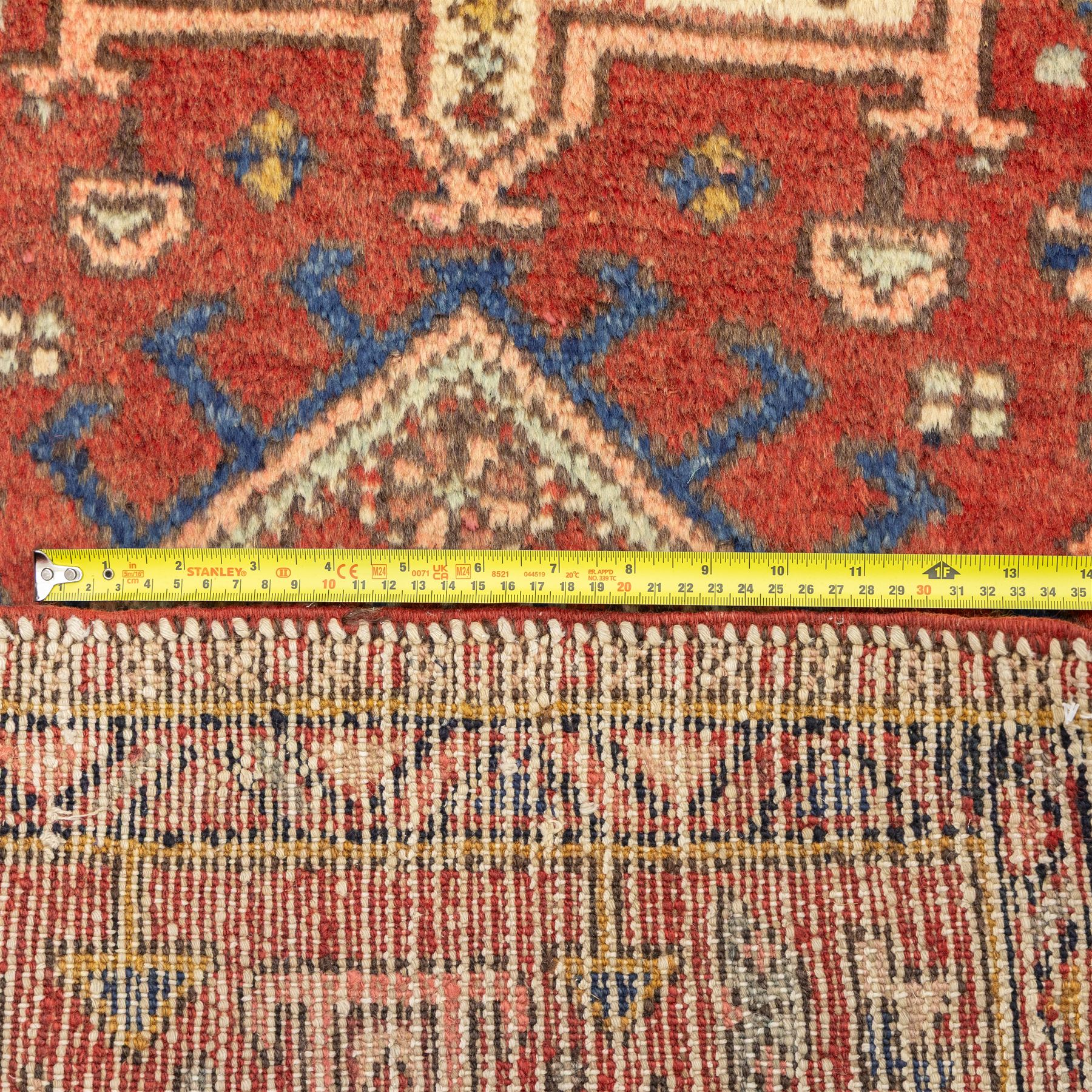 North west Persian Heriz runner, madder red field with a single column of alternating hooked and stepped lozenge medallions in ivory, blue, and terracotta, scattered with small cruciform and geometric motifs within a brick red border, angular motifs between narrow guard stripes 