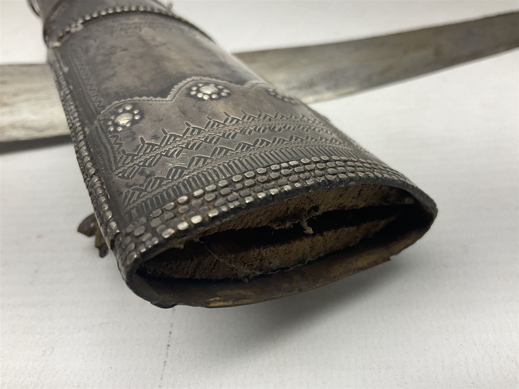 Late 19th/20th century Middle Eastern jambiya dagger the 36cm broad curved double edged steel blade with traces of script, horn and copper backed waisted white metal hilt with three roundel buttons; in ornate white metal and leather mounted brass and steel scabbard L60.5cm overall