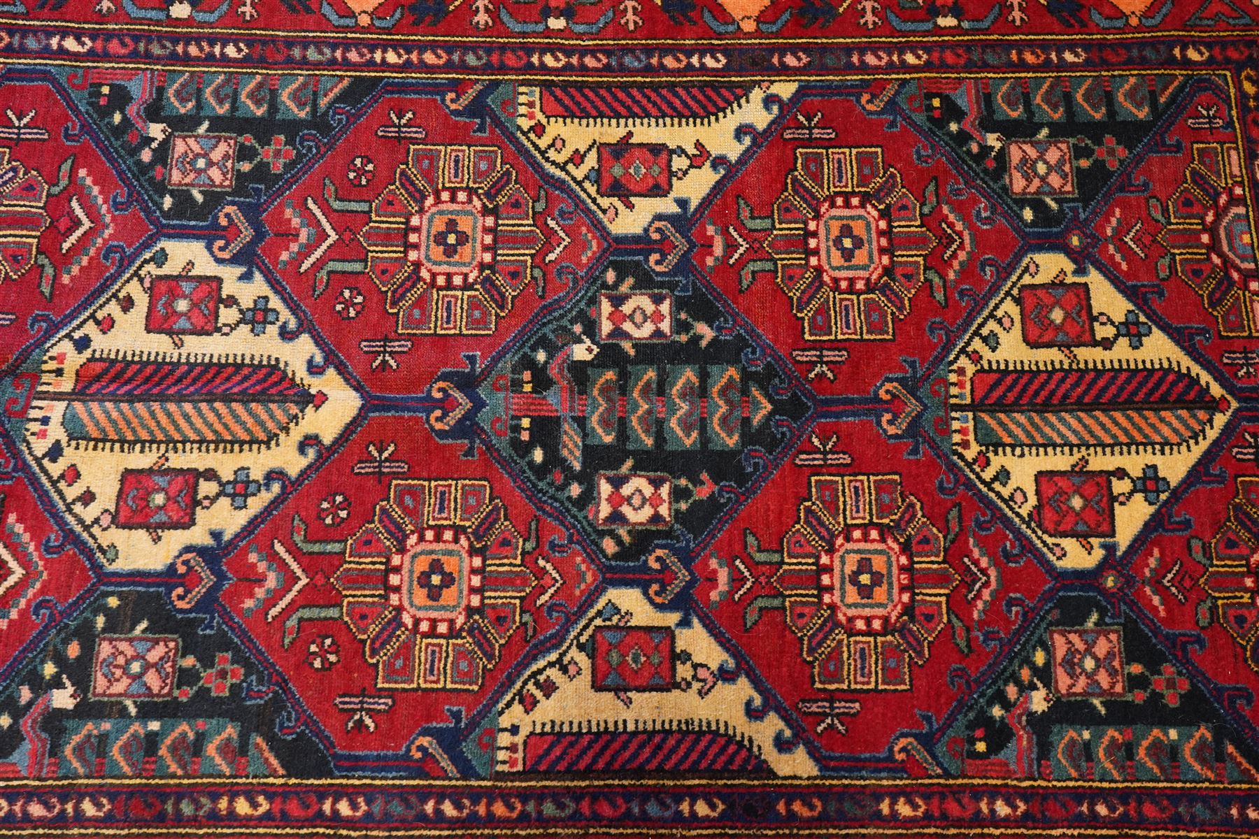 North West Persian Heriz hand-knotted rug, madder red field with an all-over lattice of stepped lozenge medallions enclosing stylized geometric floral motifs and ivory reserve panels, framed by angular vinery and motif borders, main border with with stylized rosettes and geometric devices, flanked by narrow guard stripes,, cotton fringe ends 