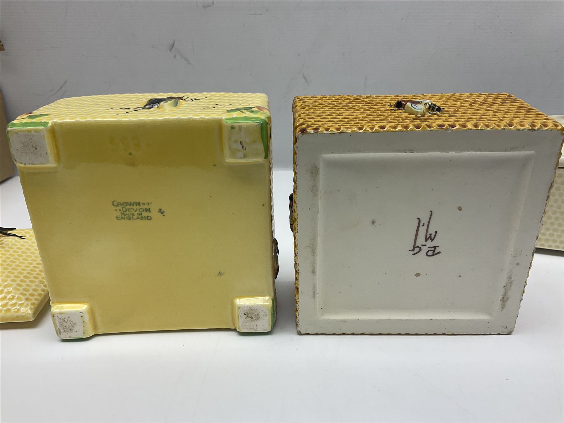 Four square honey boxes with lids,  each decorated with honeycomb pattern and finished with a bee finial