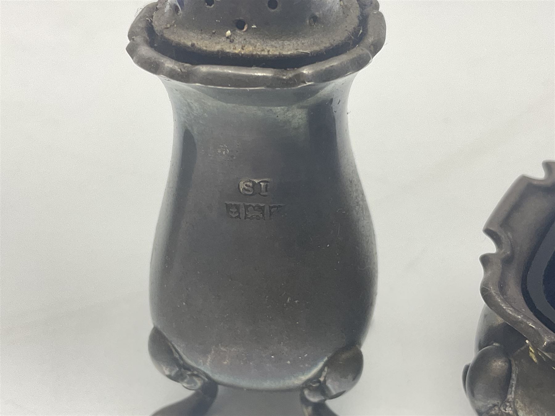 Modern two piece silver cruet set, comprising pepper shaker and open salt, each with shaped rims and upon four pad feet, hallmarked William Suckling Ltd, Birmingham 1962, together with an early 20th century silver open salt, of oval form, hallmarked William Aitken, Birmingham 1918