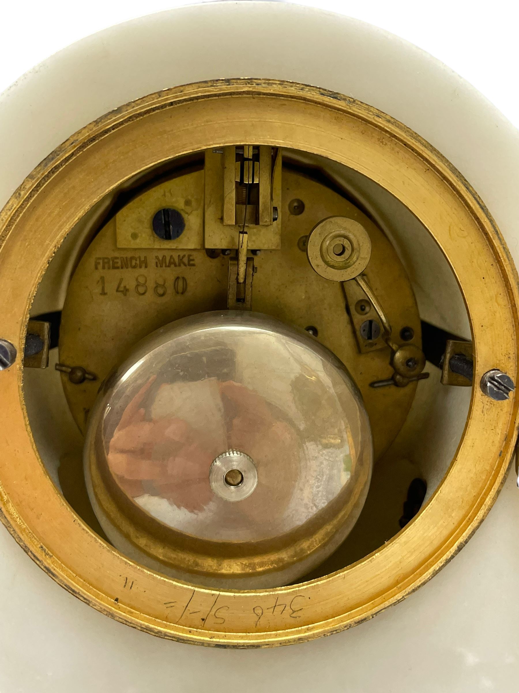An early 20th century white marble mantle clock in a break front case with an arched top and finial, gilded scroll work to the sides and pierced foliate panels to the front, plinth raised on five bun feet, enamel dial with garland decoration, Arabic numerals, minute markers and Louis XV gilt hands, within a convex glazed bezel, eight-day Parisian striking movement striking the hours and half hours on a bell, with two conforming single light candlesticks. With Pendulum.

