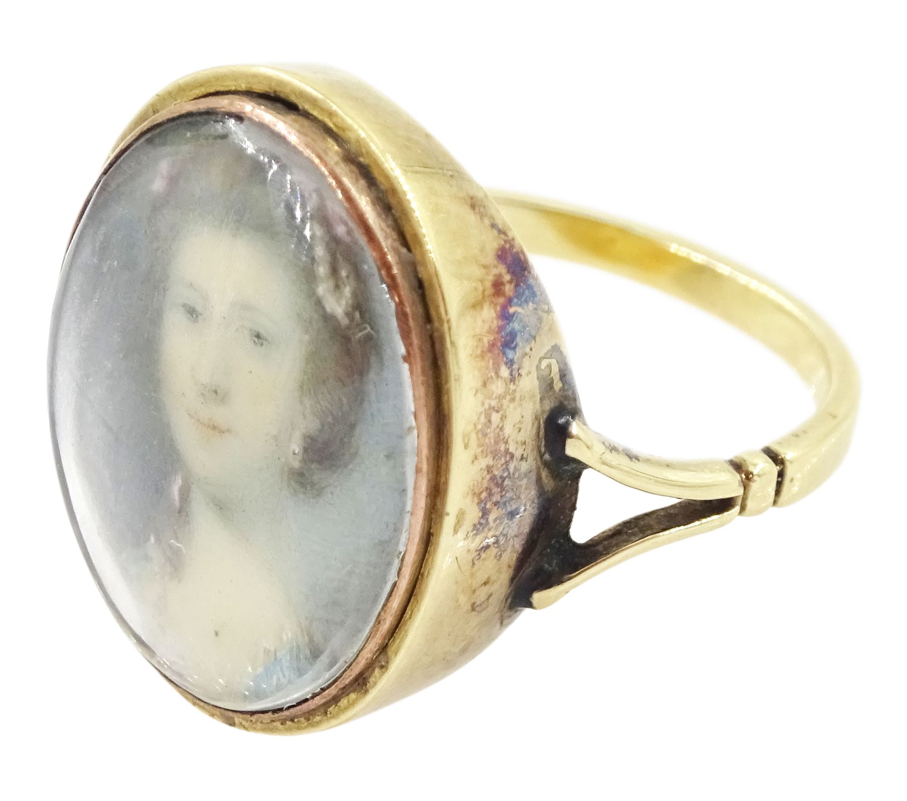 19th century gold portrait ring, set with an oval miniature of a woman wearing a pearl hairpin and earrings on ivory, under a glazed panel, set into a later gold ring with split shoulders. This lot has been registered for sale under Section 10 of the APHA Ivory Act