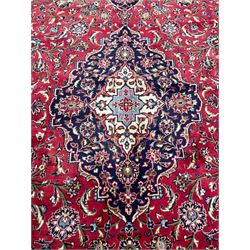 Central Persian Kashan crimson ground carpet, central  floral pole medallion with matching spandrels within a field of scrolling palmette motifs and foliage, the heavily banded indigo border with repeating plant motifs interlaced with scrolled branches