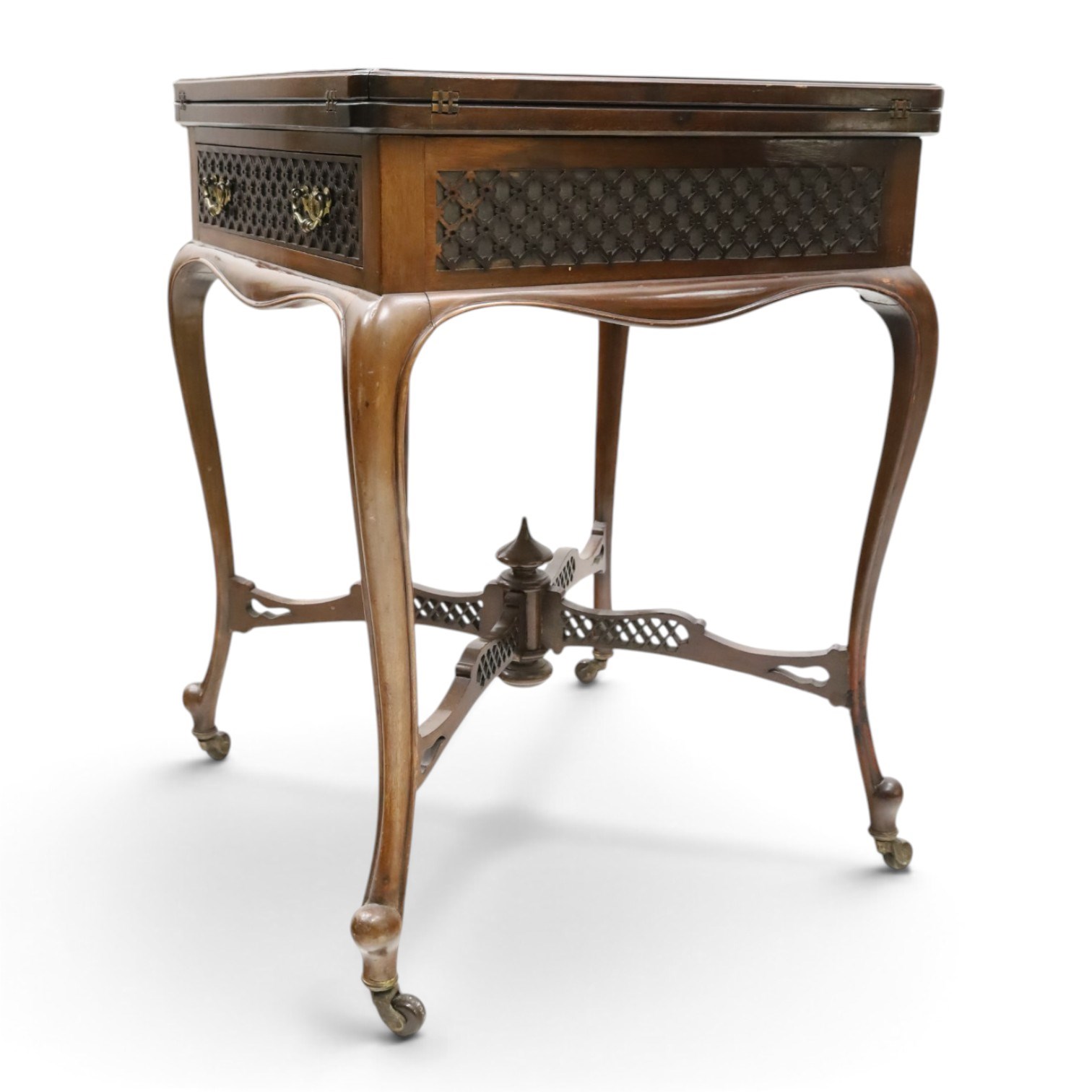 Edwardian carved mahogany envelope card table, the rectangular quadruple hinged top enclosing baize-lined interior, the single frieze drawer and sides with blind-fretwork carving, over cabriole supports with scroll feet and castors united by pierced lattice fretwork X-stretcher with turned finial
