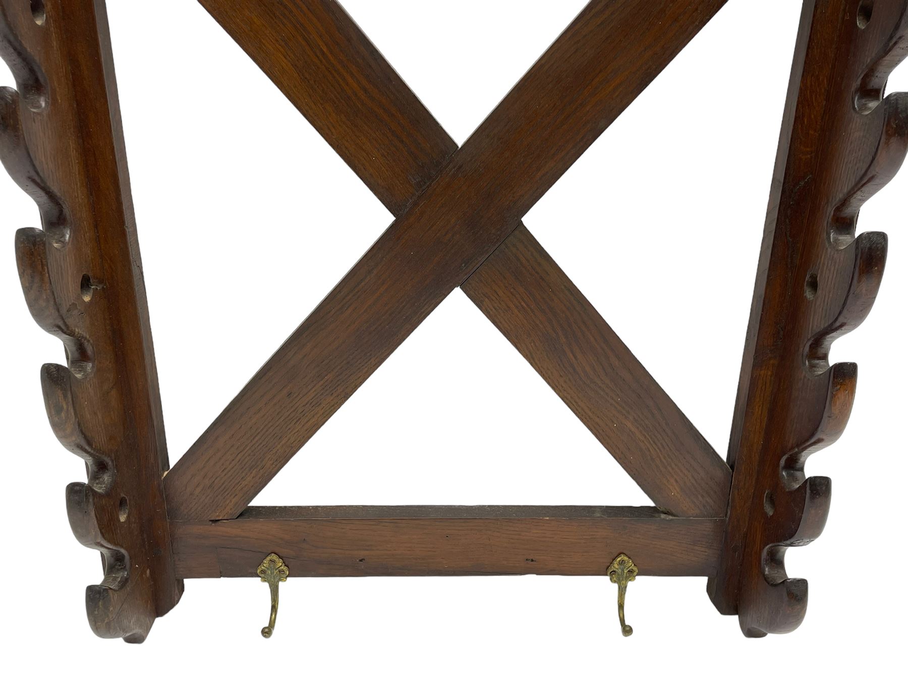 Victorian oak wall hanging whip or stick rack, sloped arch pediment carved with central grotesque mask with extended scrolling foliage, the upright supports cut with rests, x-framed back, two lower hooks