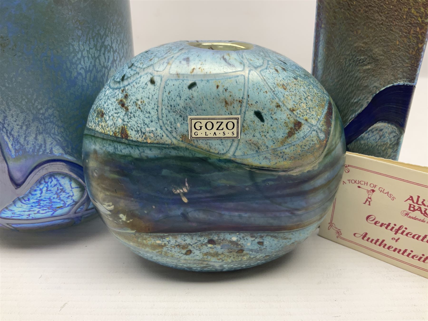 Two Isle of White glass vases, by Alum Bay Glass, both with blue swirl design upon an iridescent mottled blue/green ground, together with a Gozo Glass vase of pebble form, with similar design, H12cm