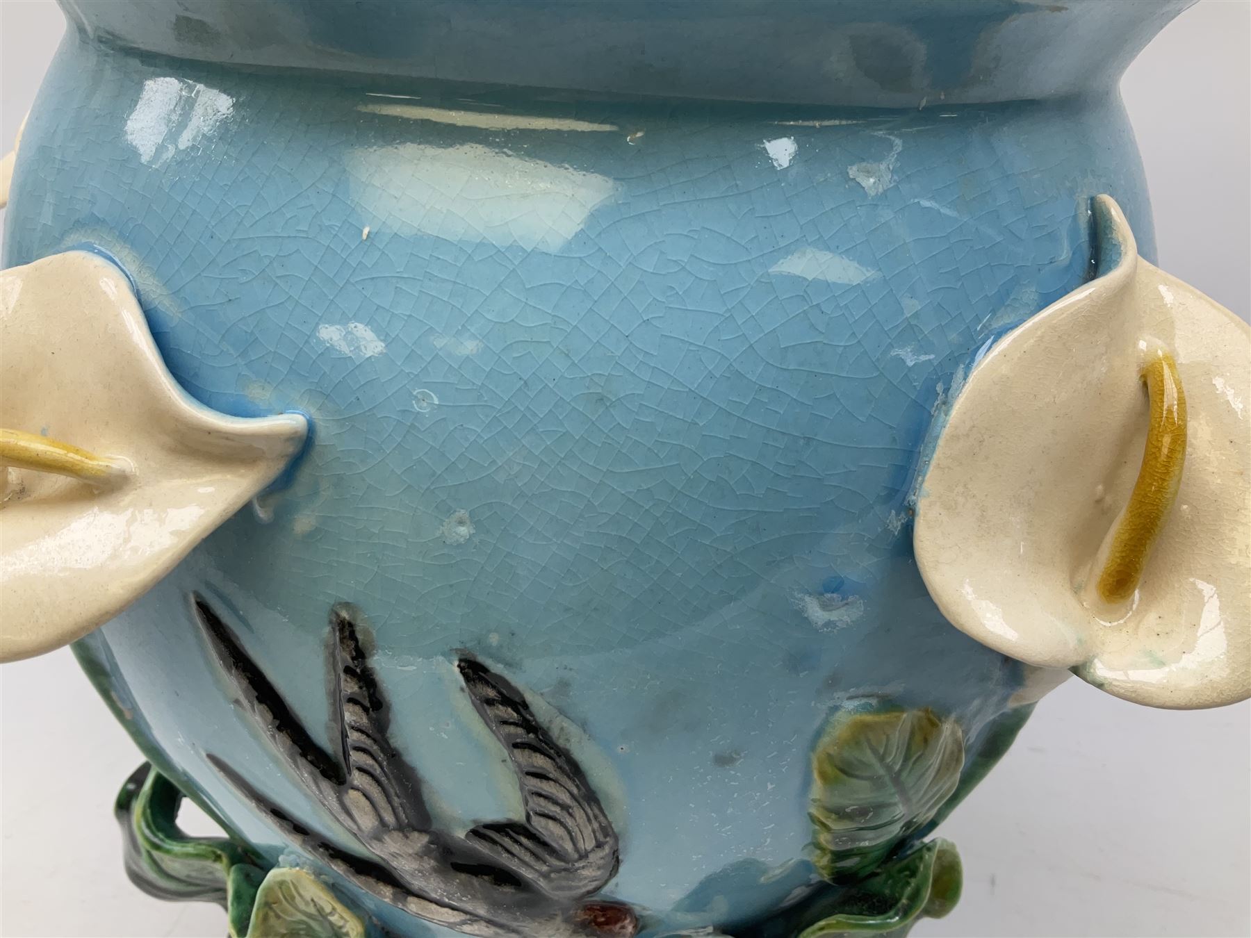 George Jones style majolica jardiniere of globular form, supported on four feet formed from modelled lily leaves growing up the side of the pot, with swallows flying amongst the white lily flowers, all set against a blue ground, with a pink interior, H27cm