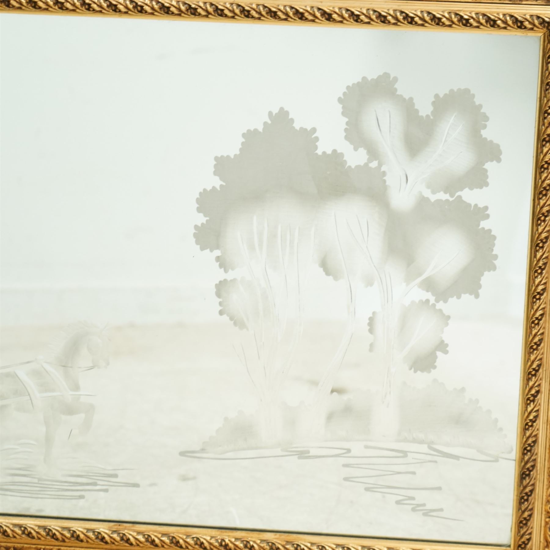 20th century giltwood and gesso wall mirror, rectangular form with pierced foliate and scroll moulded frame, rope twist inner moulding, enclosing an engraved mirror plate decorated with a horse drawn carriage and stylised trees