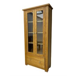Light oak bookcase display cabinet, projecting square cornice over glazed double doors enclosing three adjustable shelves, single drawer base, on stile supports