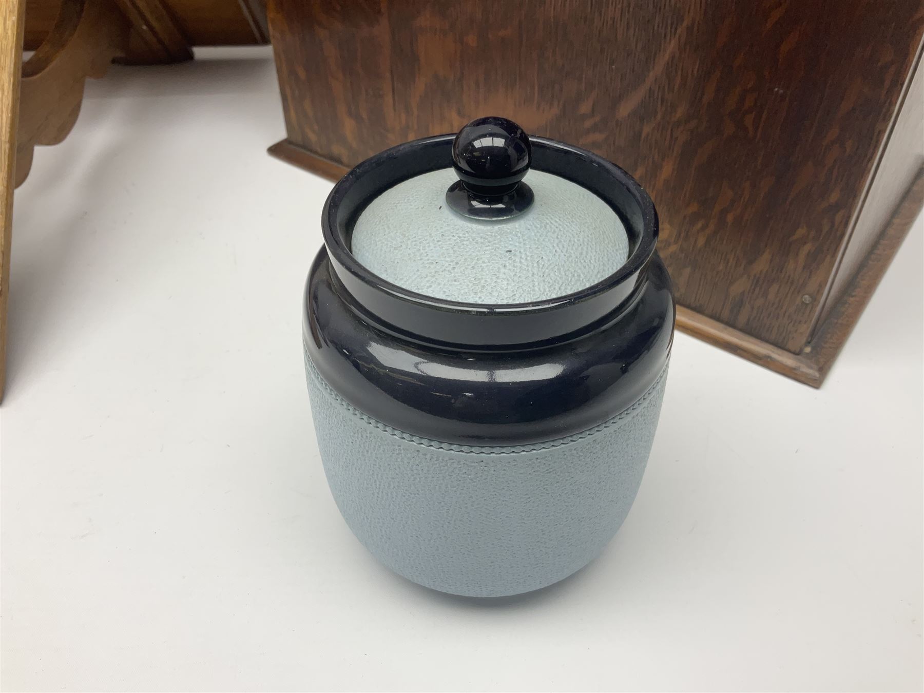 Early 20th century oak smokers cabinet, with brass shield shaped mounts, opening to reveal a compartmentalised interior with three drawers, pipe rack and tobacco jar, together with a small wooden shelf, smokers cabinet H28.5cm