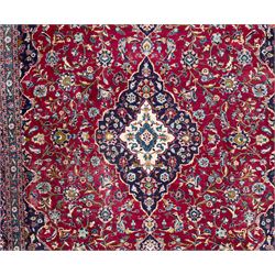 Pair of Persian wool rugs, each with rich red ground, one centred with a diamond-shaped medallion and navy spandrels within a floral field, the other with radiating floral medallion and scrolling foliate motifs, both enclosed by multiple borders with palmette and flowerhead designs, from the region of Kashan 291x376, 299 x 378 